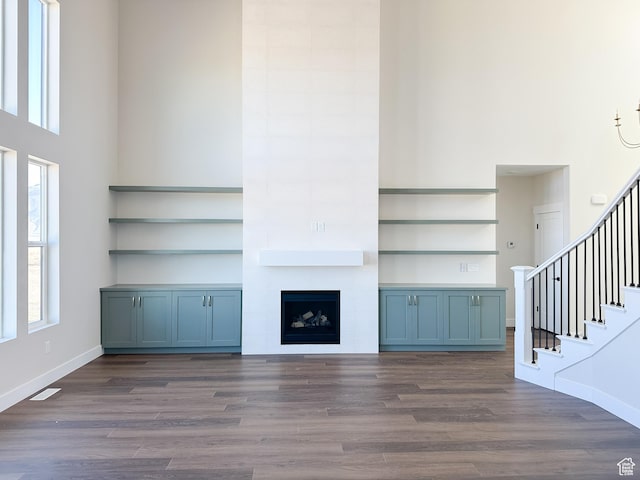 unfurnished living room featuring a high ceiling, baseboards, stairs, and wood finished floors