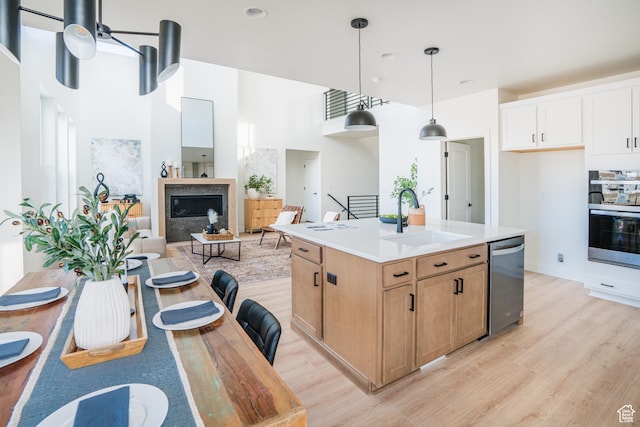 kitchen with oven, stainless steel dishwasher, light wood finished floors, pendant lighting, and a sink