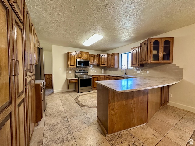 kitchen featuring decorative backsplash, stainless steel appliances, a peninsula, brown cabinetry, and glass insert cabinets