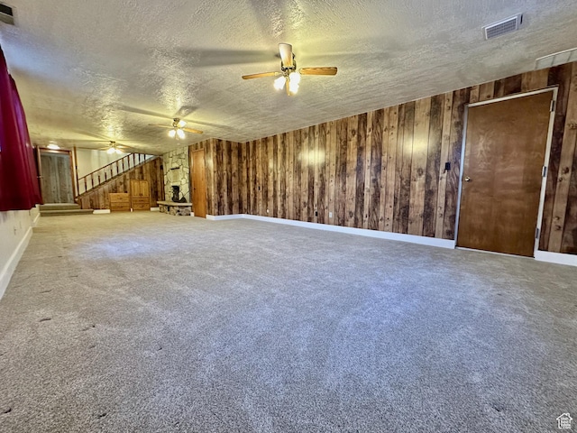 carpeted empty room featuring stairway, a ceiling fan, visible vents, wood walls, and a textured ceiling