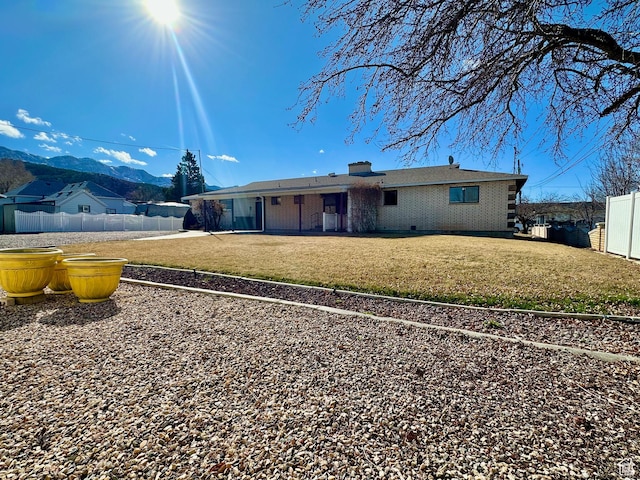back of property with a mountain view, a lawn, a chimney, and fence