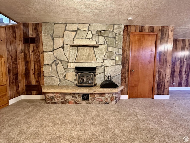 unfurnished living room featuring carpet floors, a textured ceiling, wood walls, and a fireplace