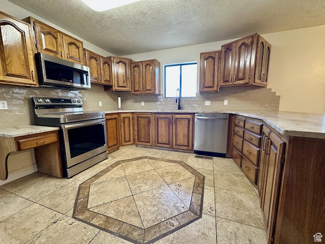kitchen featuring decorative backsplash, brown cabinets, appliances with stainless steel finishes, a textured ceiling, and a sink