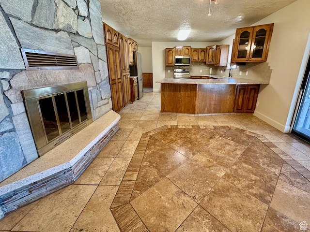kitchen with brown cabinets, appliances with stainless steel finishes, a peninsula, glass insert cabinets, and baseboards
