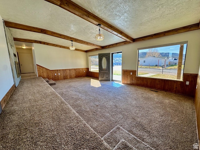 carpeted spare room featuring beam ceiling, wooden walls, a wainscoted wall, and a textured ceiling
