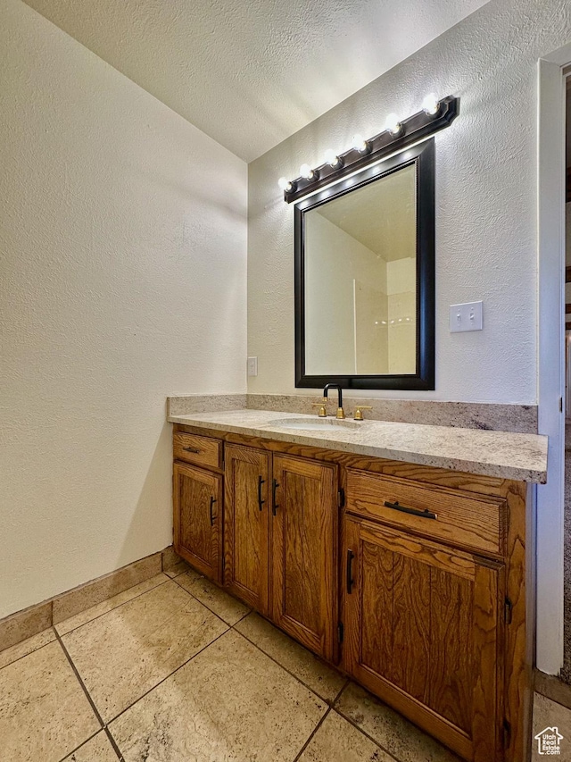 bathroom with vanity, a textured wall, baseboards, and a textured ceiling