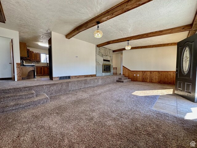 unfurnished living room featuring visible vents, carpet, a wainscoted wall, beam ceiling, and a textured ceiling
