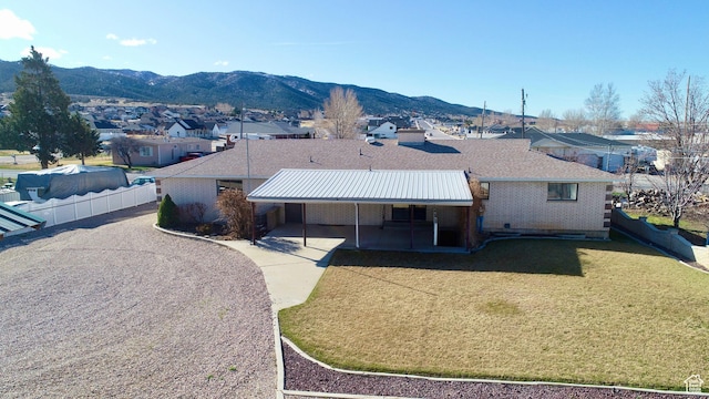 exterior space featuring brick siding, fence, a residential view, a lawn, and a mountain view