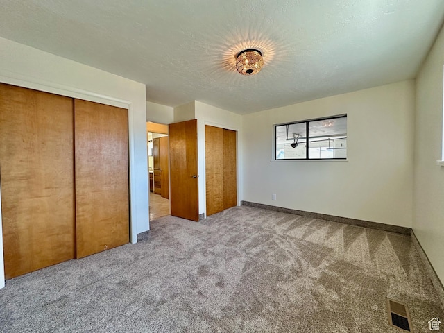 unfurnished bedroom with baseboards, visible vents, carpet floors, multiple closets, and a textured ceiling