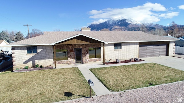 single story home featuring driveway, brick siding, a front lawn, a garage, and a mountain view