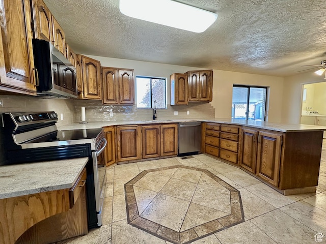 kitchen with brown cabinetry, a peninsula, a sink, decorative backsplash, and stainless steel appliances