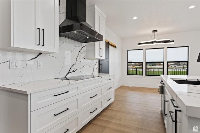 kitchen featuring light wood finished floors, white cabinets, wall chimney range hood, black electric cooktop, and backsplash