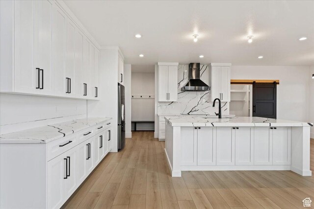 kitchen with a sink, wall chimney range hood, white cabinetry, freestanding refrigerator, and light wood finished floors