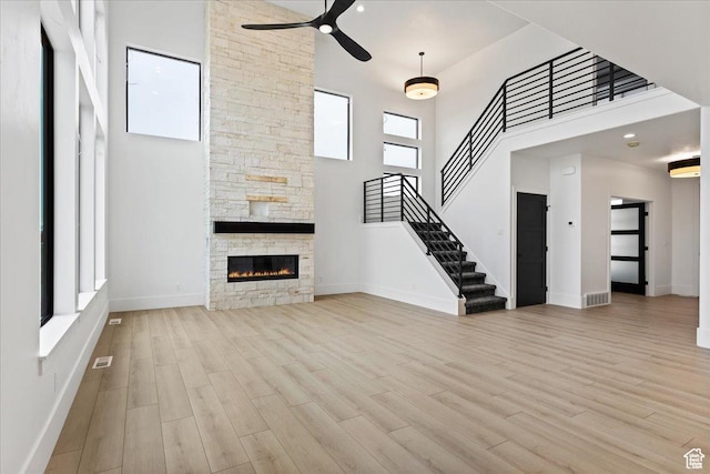 unfurnished living room featuring stairway, wood finished floors, a ceiling fan, baseboards, and a fireplace