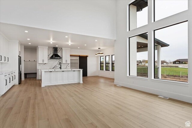 kitchen featuring light wood finished floors, backsplash, open floor plan, a barn door, and wall chimney exhaust hood