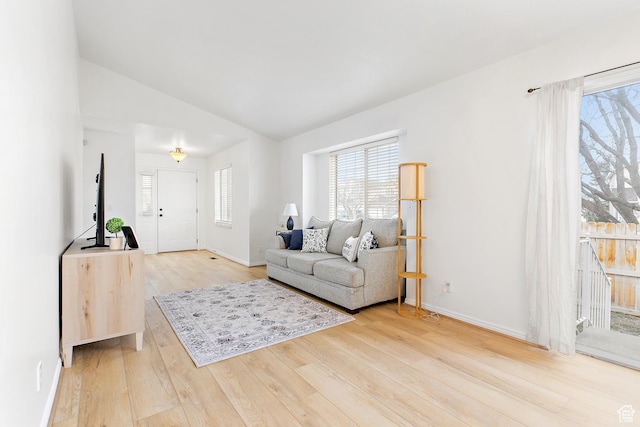 living area featuring lofted ceiling, light wood-style floors, and baseboards