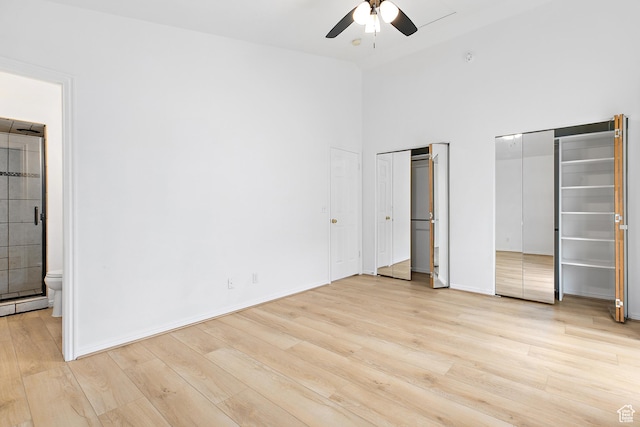 unfurnished bedroom featuring two closets, high vaulted ceiling, connected bathroom, light wood finished floors, and baseboards