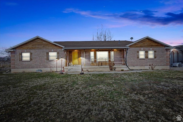 ranch-style home featuring covered porch, brick siding, and a yard