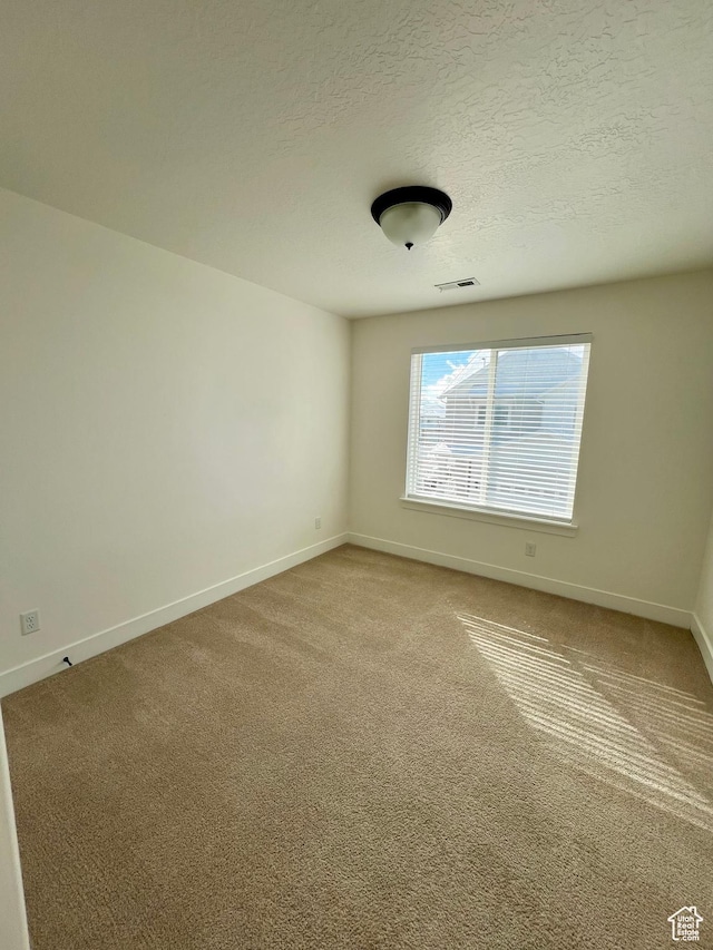 empty room featuring visible vents, baseboards, light colored carpet, and a textured ceiling