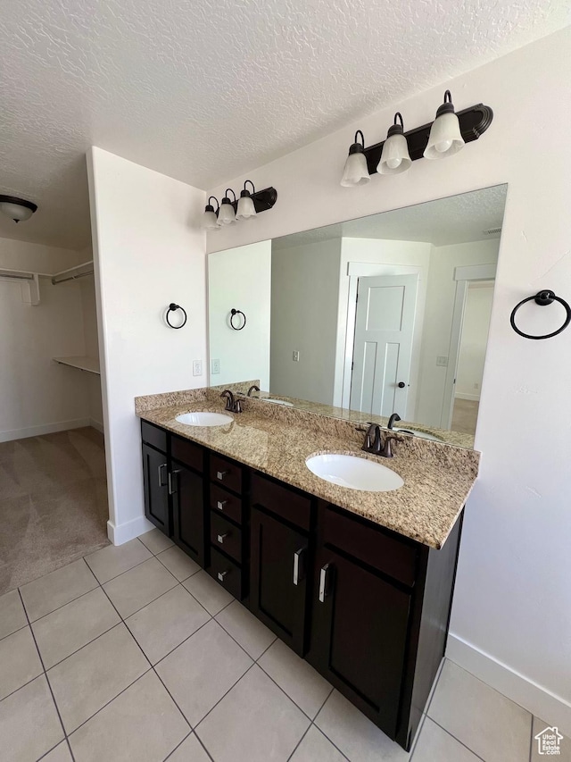 bathroom with a sink, a walk in closet, double vanity, and tile patterned floors