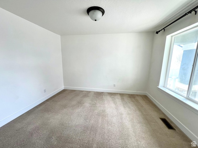 spare room with a textured ceiling, baseboards, visible vents, and light carpet
