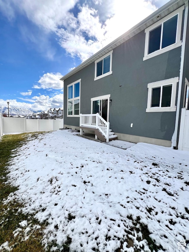 snow covered rear of property with stucco siding and fence