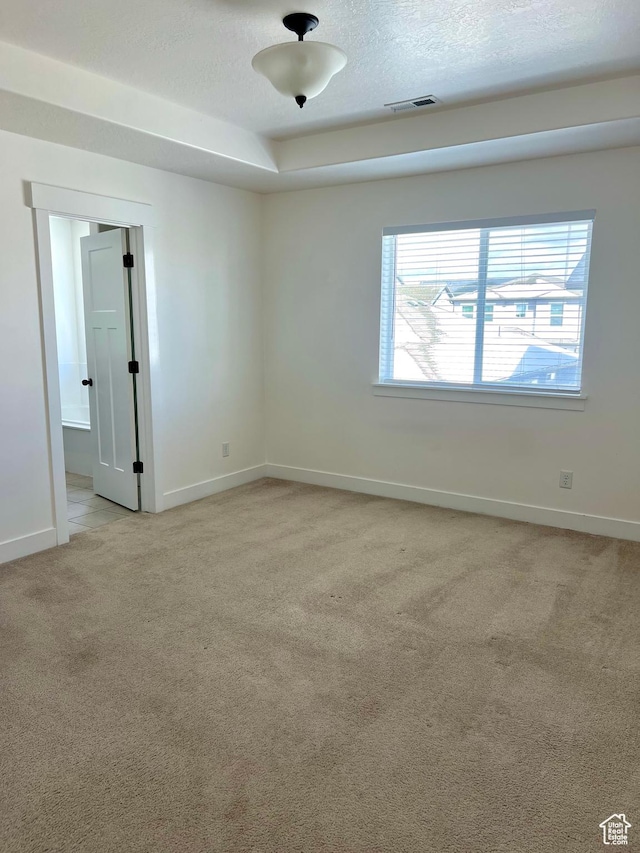 spare room featuring a textured ceiling, baseboards, visible vents, and light carpet