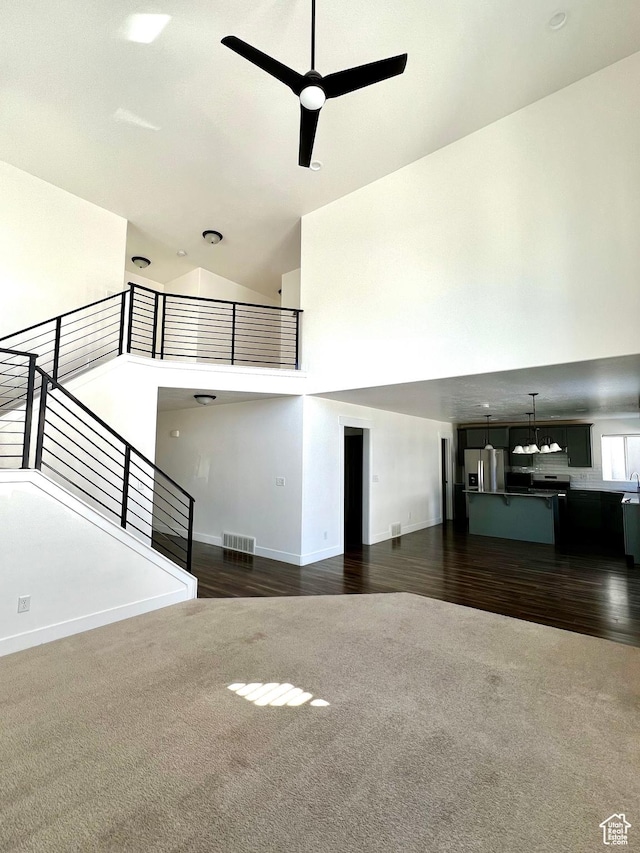 unfurnished living room featuring visible vents, a high ceiling, ceiling fan, and carpet