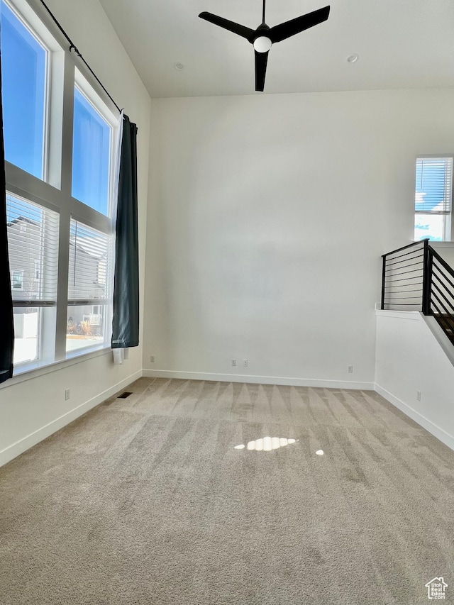 empty room with visible vents, light colored carpet, baseboards, and ceiling fan
