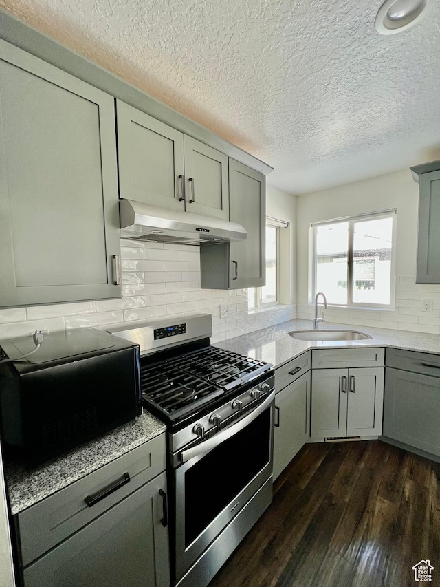 kitchen with gray cabinetry, a sink, under cabinet range hood, stainless steel gas range, and dark wood-style flooring