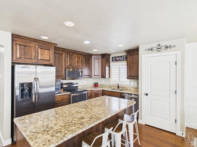 kitchen featuring light stone countertops, a sink, stainless steel appliances, dark wood-type flooring, and a kitchen island