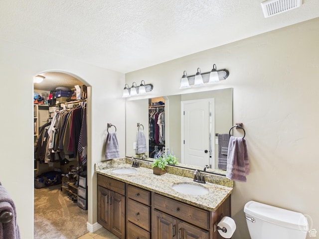 full bathroom featuring visible vents, toilet, a textured ceiling, and a sink