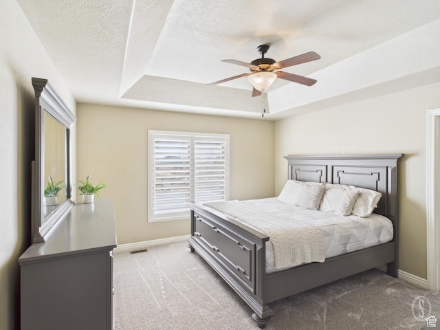 carpeted bedroom with a ceiling fan, a tray ceiling, a textured ceiling, and baseboards