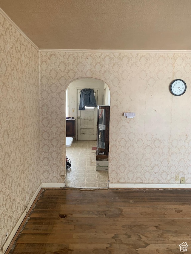 hallway with wood finished floors, wallpapered walls, arched walkways, ornamental molding, and a textured ceiling
