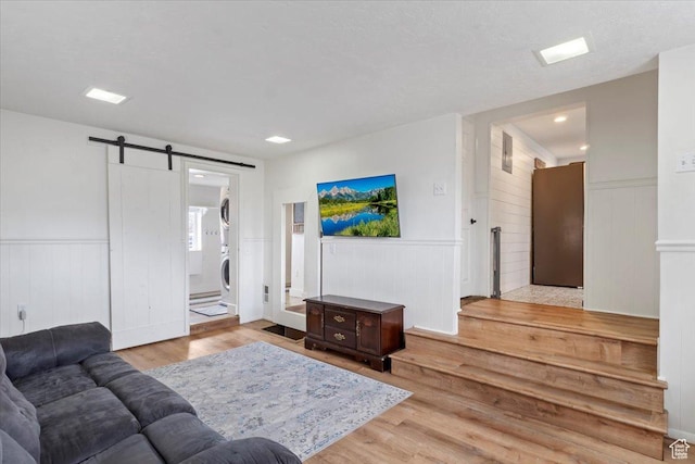 living area with a barn door, a wainscoted wall, wood finished floors, and stacked washing maching and dryer
