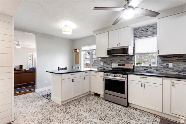 kitchen featuring a peninsula, ceiling fan, decorative backsplash, appliances with stainless steel finishes, and dark countertops