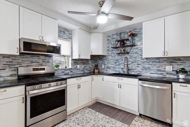 kitchen featuring dark countertops, stainless steel appliances, white cabinetry, a ceiling fan, and a sink