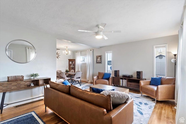 living area featuring visible vents, ceiling fan with notable chandelier, a textured ceiling, and wood finished floors