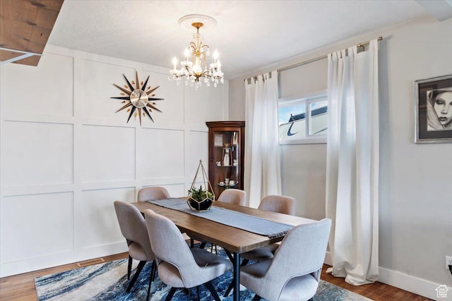 dining room with an inviting chandelier, a decorative wall, wood finished floors, and baseboards
