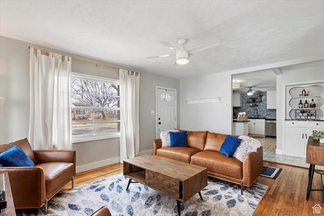 living area featuring baseboards, a textured ceiling, light wood-type flooring, and ceiling fan