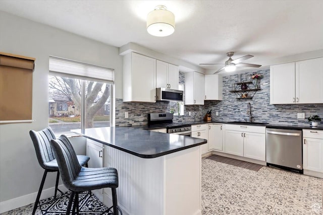 kitchen with a ceiling fan, a sink, tasteful backsplash, dark countertops, and stainless steel appliances
