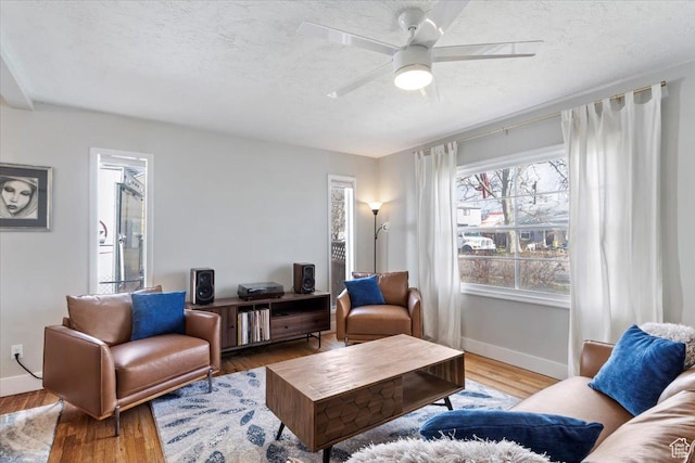 living area featuring ceiling fan, baseboards, a textured ceiling, and wood finished floors