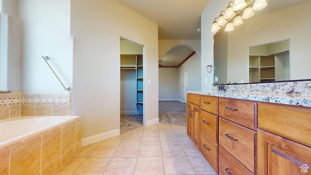 bathroom with tile patterned floors, vanity, a walk in closet, and tiled tub