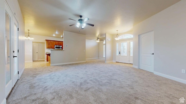 unfurnished living room with light colored carpet, ceiling fan with notable chandelier, and baseboards