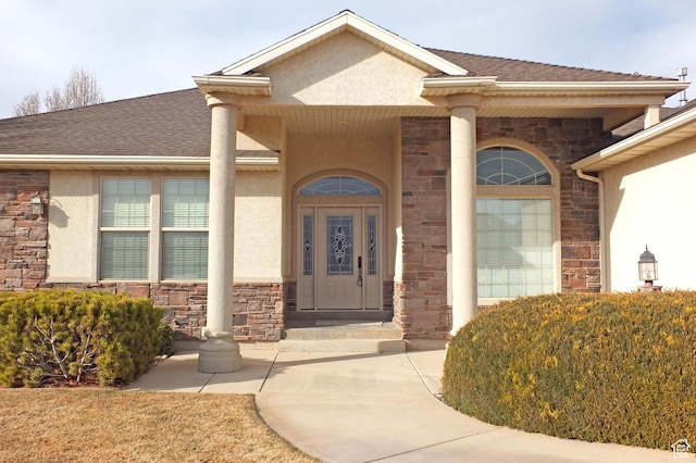 entrance to property with stucco siding, stone siding, and a shingled roof