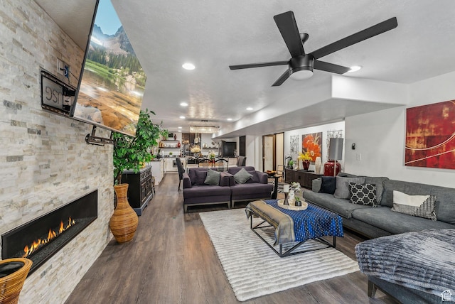 living room with a stone fireplace, a textured ceiling, a ceiling fan, and wood finished floors