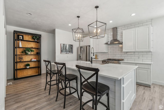 kitchen with stainless steel refrigerator with ice dispenser, wall chimney exhaust hood, light wood finished floors, range, and light countertops