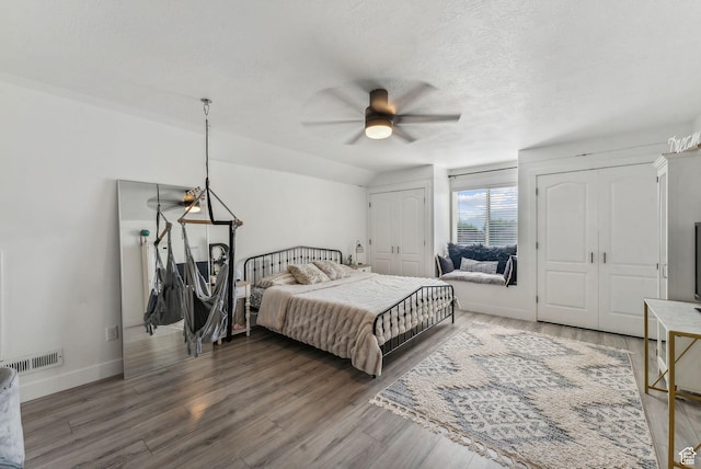bedroom with visible vents, baseboards, multiple closets, wood finished floors, and a textured ceiling
