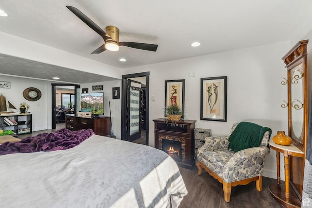 bedroom with recessed lighting, wood finished floors, a warm lit fireplace, and ceiling fan