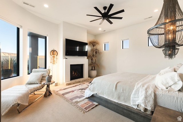 carpeted bedroom with recessed lighting, visible vents, a warm lit fireplace, and ceiling fan with notable chandelier